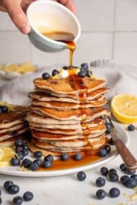 A stack of lemon blueberry pancakes with syrup pouring over the top.