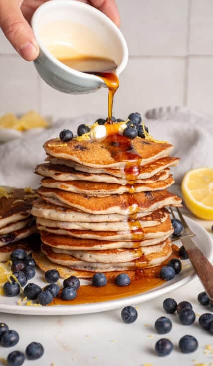 A stack of lemon blueberry pancakes with syrup pouring over the top.
