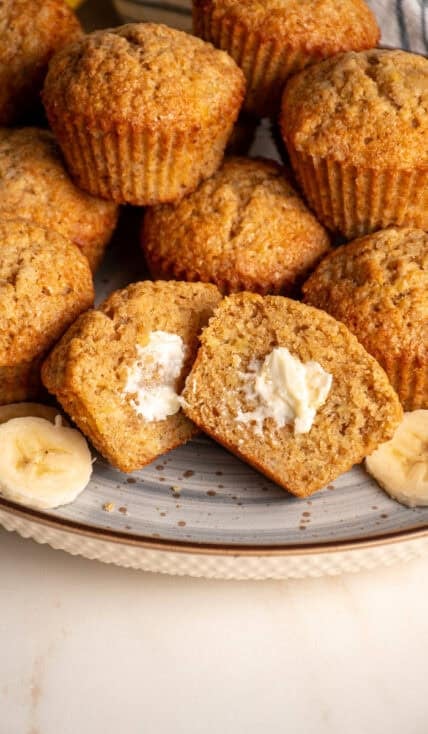 A plate filled with whole wheat banana muffins with one in the center cut in half.