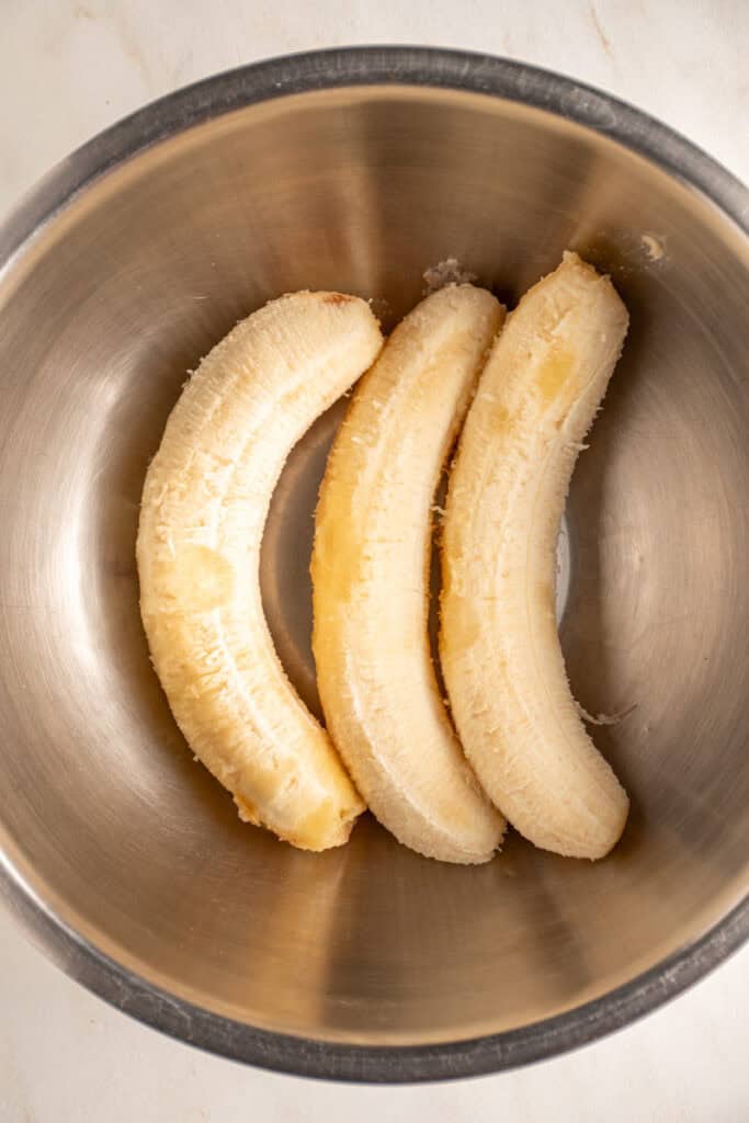 Three large ripe bananas in a mixing bowl.