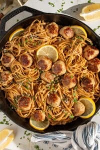 A large skillet filled with pasta and golden brown chicken piccata meatballs.