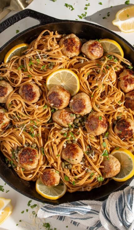 A large skillet filled with pasta and golden brown chicken piccata meatballs.