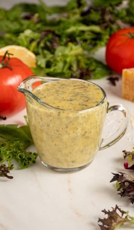 A serving glass filled with homemade Italian Dressing surrounded by lettuce.