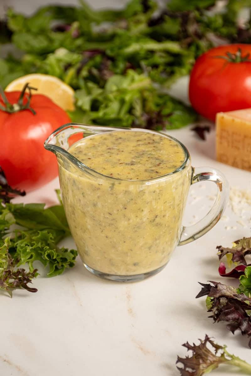 A serving glass filled with homemade Italian Dressing surrounded by lettuce.