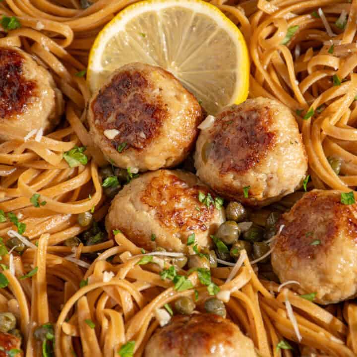 A close up of pasta and chicken piccata meatballs with capers.