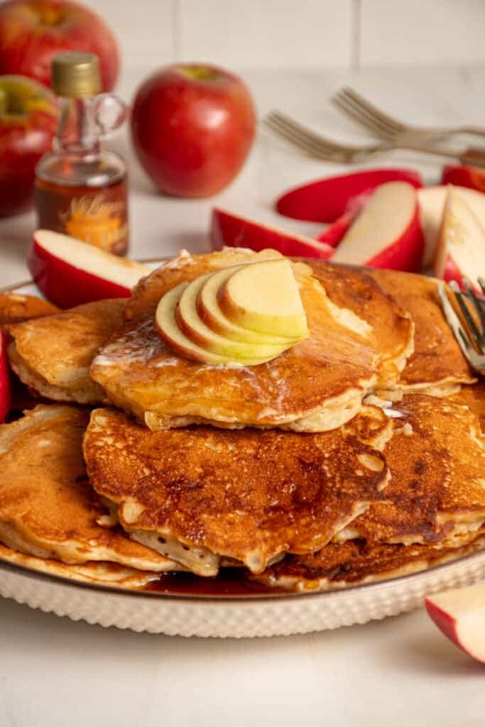 A stack of apple pancakes on a plate with fresh slices of apple on top.
