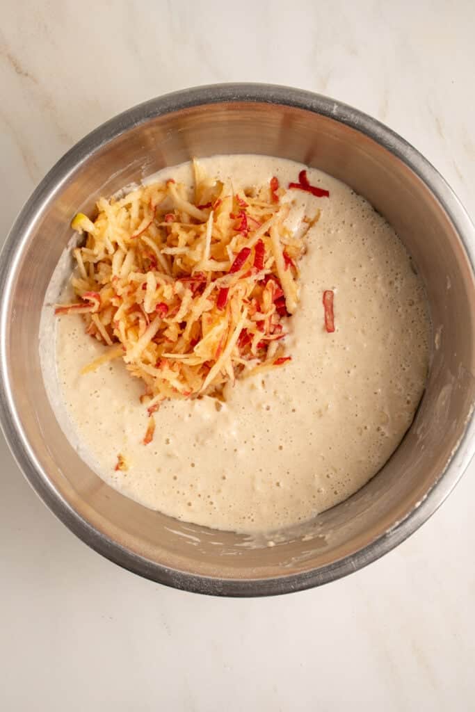 Grated apple being added to pancake batter.