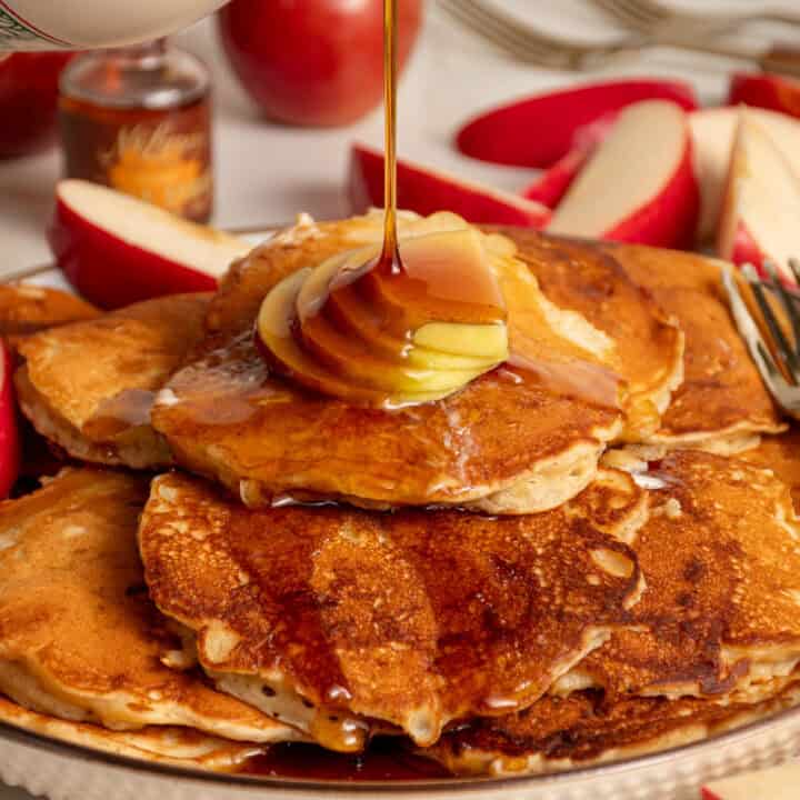 A plate full of apple pancakes topped with apple slices and maple syrup.