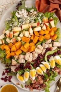 A platter with Fall Cobb Salad with butternut squash, roast chicken, dried cranberries, and pumpkin seeds.