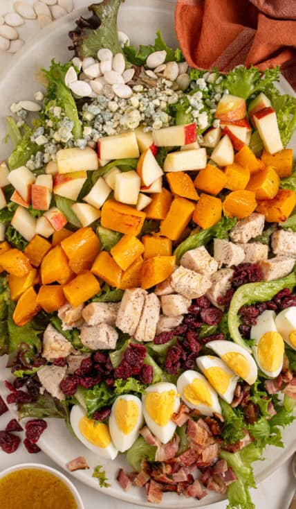 A platter with Fall Cobb Salad with butternut squash, roast chicken, dried cranberries, and pumpkin seeds.