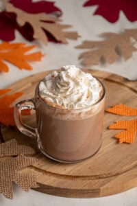 A clear glass mug with pumpkin hot chocolate and topped with whipped cream.