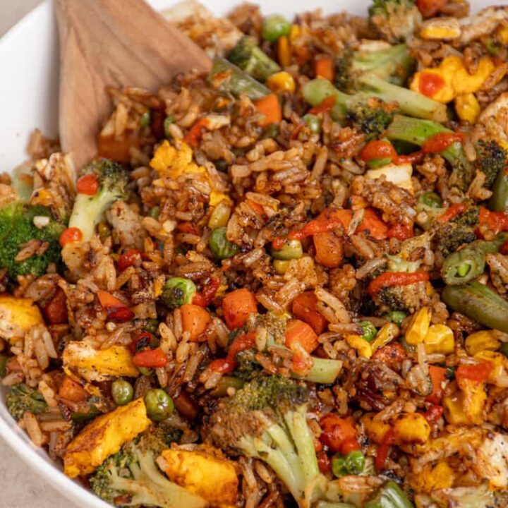 A large white bowl filled with frozen veggie fried rice drizzled with sriracha.