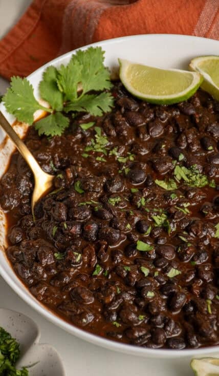 A white bowl filled with cooked black beans garnished with fresh cilantro.